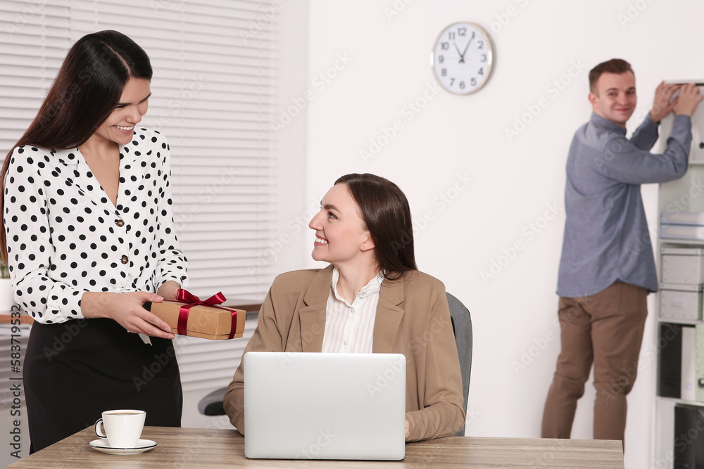 Woman presenting gift to her colleague in office Woman presenting gift to her colleague in office