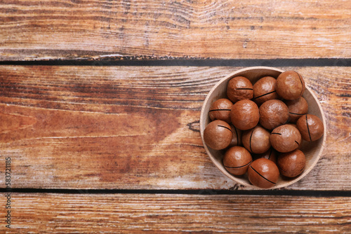 Delicious organic Macadamia nuts in bowl on wooden table, top view. Space for text