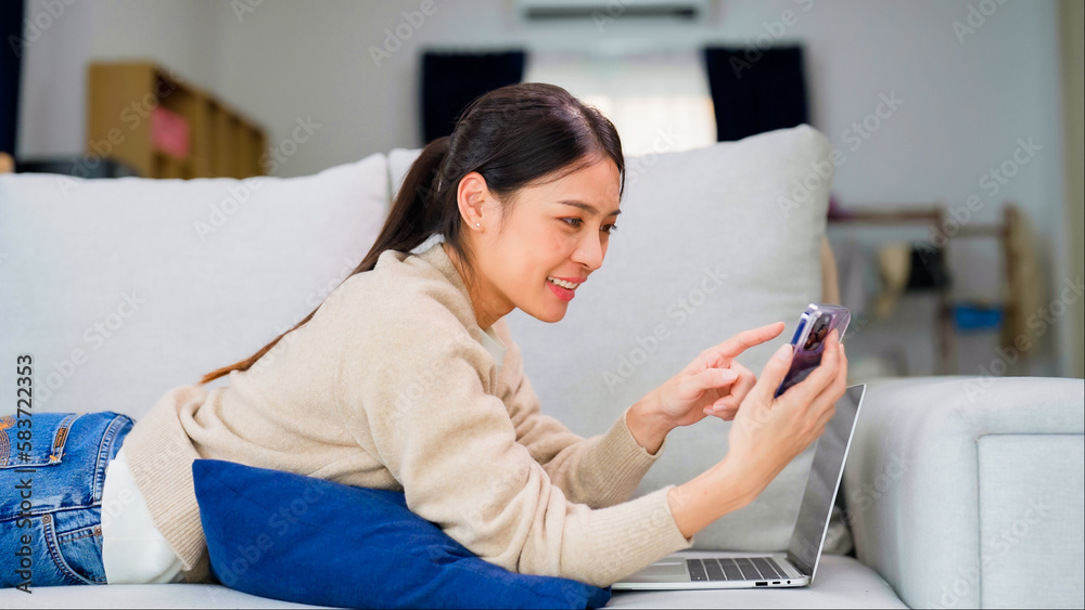 Young asian woman using smart phone at home. Smiling female making video call meeting smartphone at house, messaging or browsing social networks while relaxing on couch - obrazy, fototapety, plakaty 