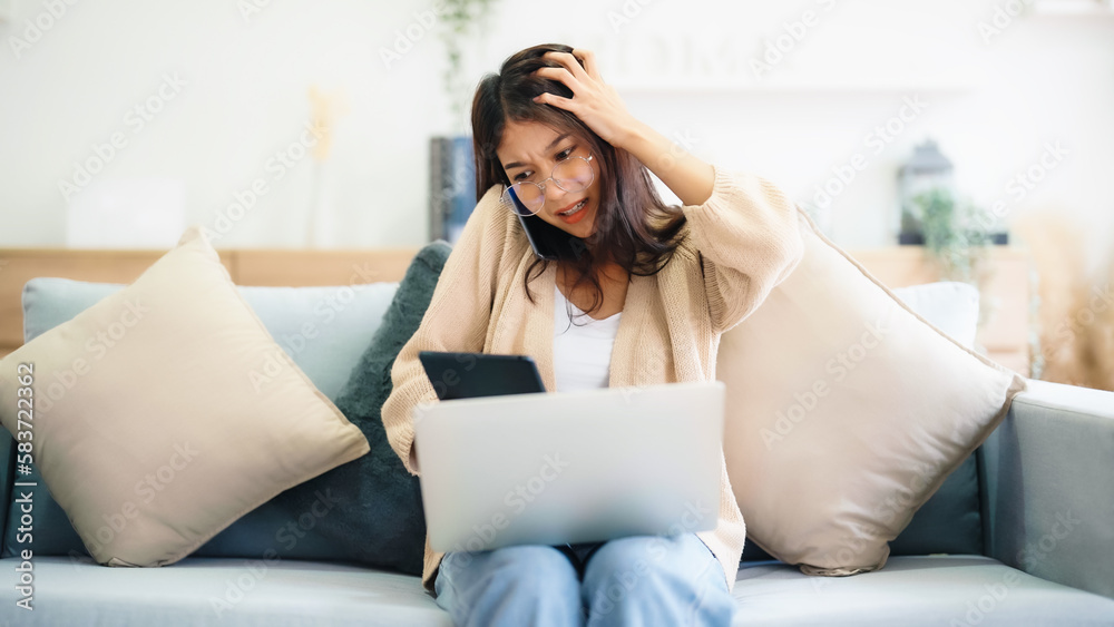 Young asian woman using computer laptop and mobile smartphone while seated on couch at home Young asian woman using computer laptop and mobile smartphone while seated on couch at home