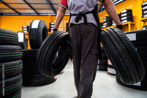 A male auto mechanic holding two tires in tire shop to change car wheels at service center or auto repair shop for auto industry. Automobile industry.