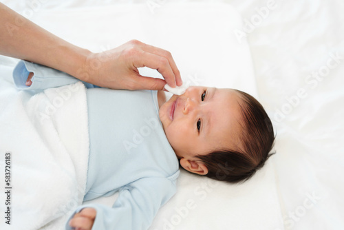 mother cleaning and wiping newborn baby face with cotton pad on bed