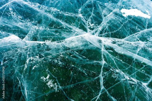 Cracked ice on a frozen lake. The natural texture of winter ice with white bubbles and cracks on a frozen lake. Abstract bright background, flat layout, layout, top view. Background. Selective focus.