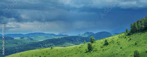Mountains and hills in stormy weather, contrasting light, summer greenery of forests and meadows, panoramic view 
