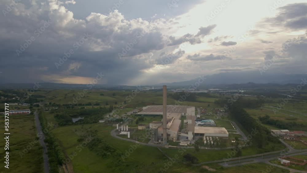 factory with a long chimney with weeds around it at sunset with heavy rain clouds for glass manufacturing factory with a long chimney with weeds around it at sunset with heavy rain clouds for glass manufacturing