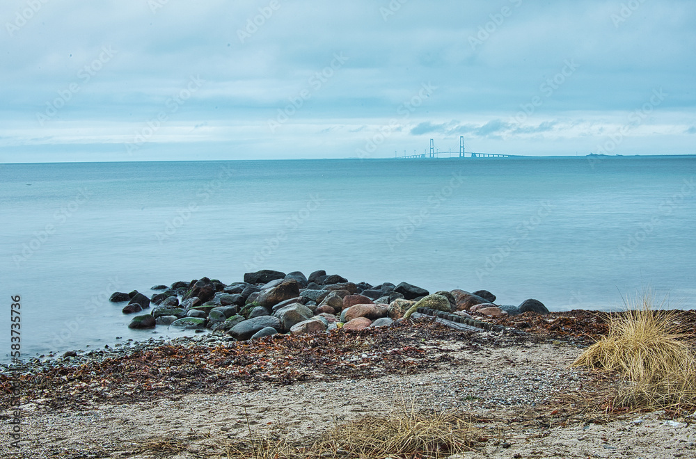 at the beach in Nyborg, Denmark. view of stones, sea and Great Belt Bridge in the back.