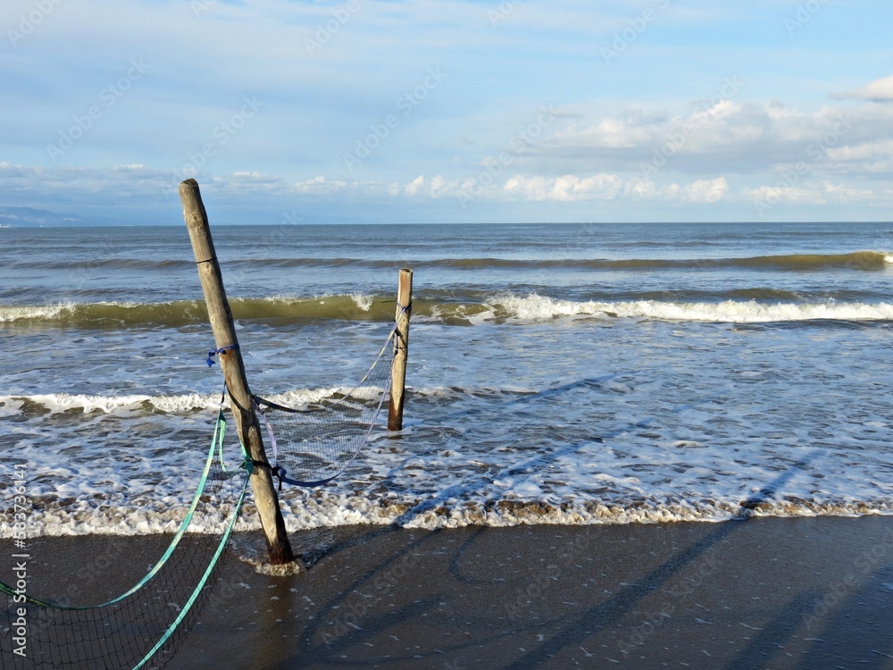 Postes de madera y red caída engullidos por el mar en una playa Postes de madera y red caída engullidos por el mar en una playa