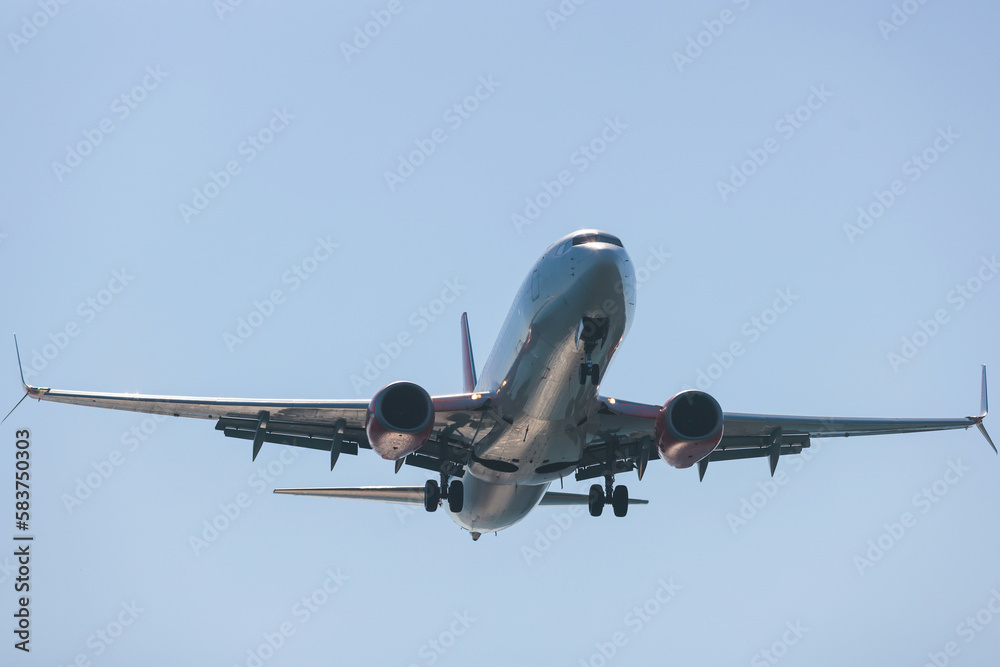 Fototapeta premium View of modern passenger plane aircraft in flight, commercial airplane flying in the sky before take off or landing, with mountains in the background in a summer sunny day