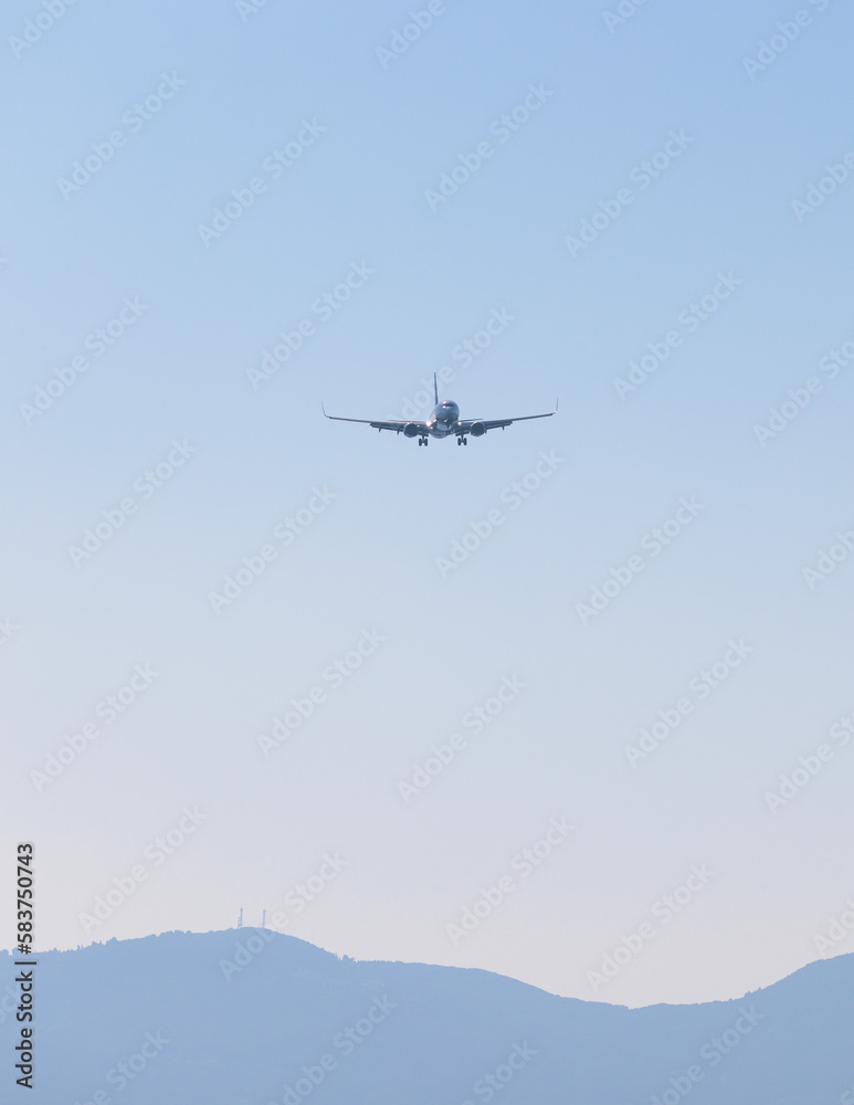 View of modern passenger plane aircraft in flight, commercial airplane flying in the sky before take off or landing, with mountains in the background in a summer sunny day View of modern passenger plane aircraft in flight, commercial airplane flying in the sky before take off or landing, with mountains in the background in a summer sunny day