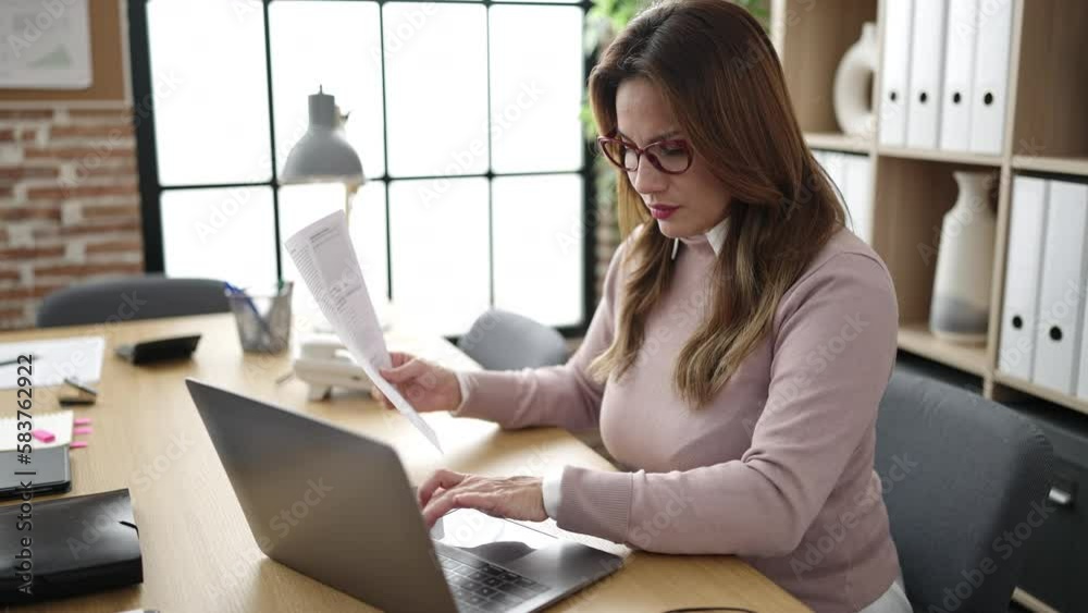 Young beautiful hispanic woman business worker using laptop reading document at office Young beautiful hispanic woman business worker using laptop reading document at office