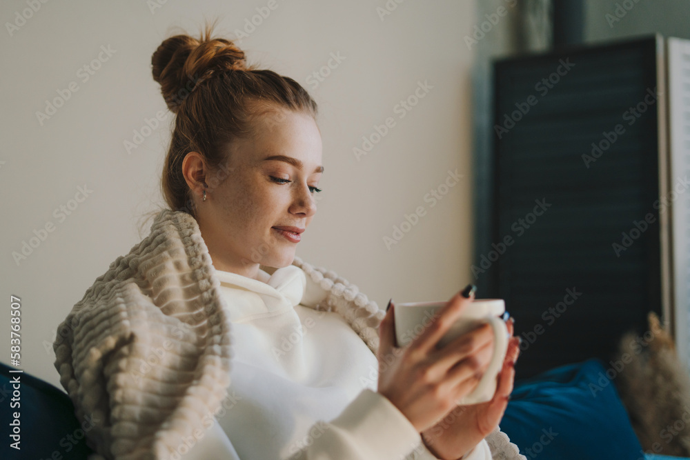 Smiling beautiful caucasian ethnicity woman resting in cozy sofa with cup of coffee in hands, enjoying carefree morning in living room. Relax, carefree, comfort Smiling beautiful caucasian ethnicity woman resting in cozy sofa with cup of coffee in hands, enjoying carefree morning in living room. Relax, carefree, comfort