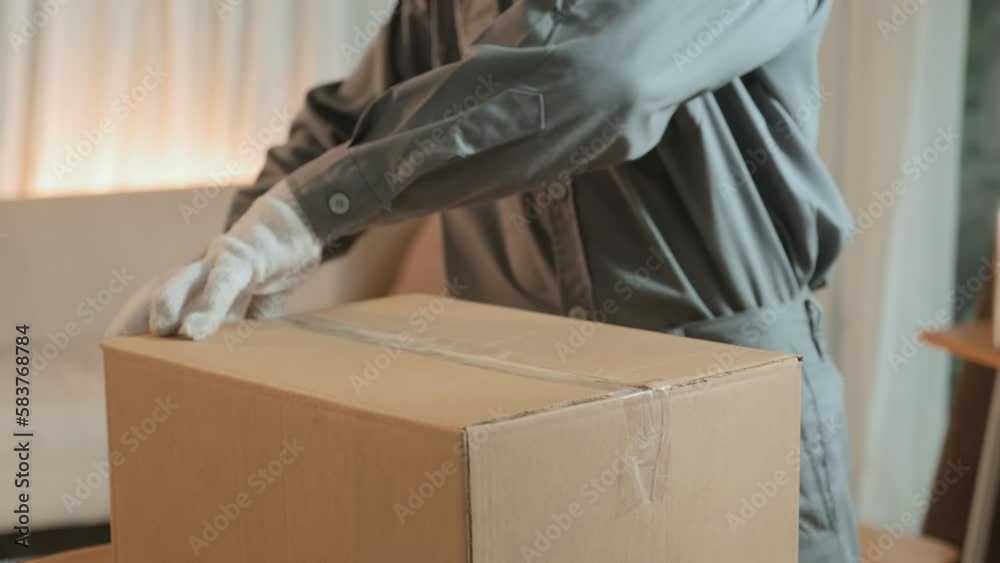 Cropped shot of moving service worker in uniform and gloves sealing carton box with transparent adhesive tape and then his colleague carrying it away from house