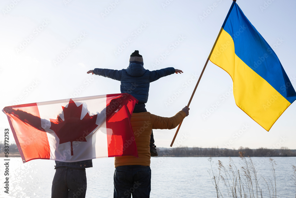 family with a child with Ukrainian and Canadian flags stand together in nature. International support and assistance to Ukraine, stop the war with Russia. problems of refugees and immigrants - obrazy, fototapety, plakaty 
