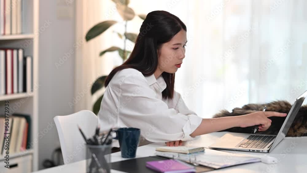 Focused college student watching distance online learning class or having virtual classroom meeting on laptop and writing on notebook Focused college student watching distance online learning class or having virtual classroom meeting on laptop and writing on notebook
