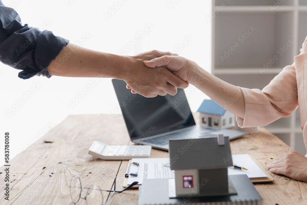 Real estate broker and customer shaking hands after signing a contract: real estate, home loan and insurance concept.