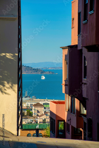 Fototapeta Naklejka Na Ścianę i Meble -  View of sailboat and mountains in sunlit background seen through shadow buildings and hills in san francisco california