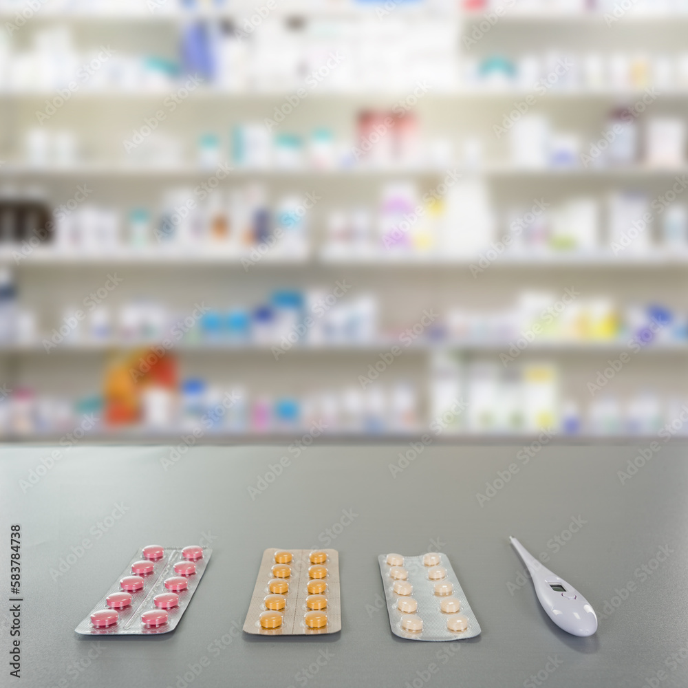 Pills and thermometer on drugstore counter with pharmacy background shelf