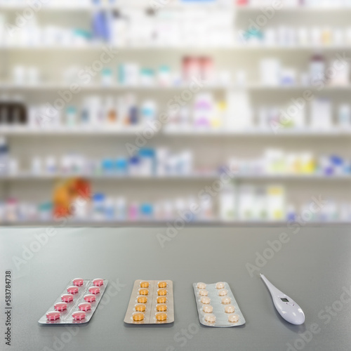 Pills and thermometer on drugstore counter with pharmacy background shelf