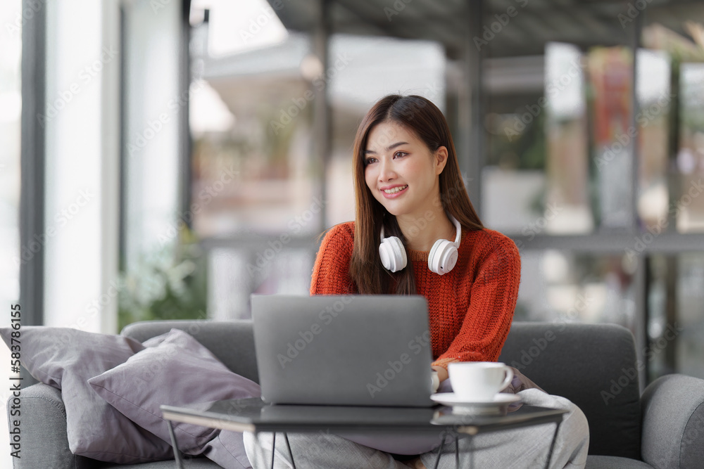 Beautiful Asian Woman smile and relaxing at home and using laptop computer sitting on cozy sofa Beautiful Asian Woman smile and relaxing at home and using laptop computer sitting on cozy sofa