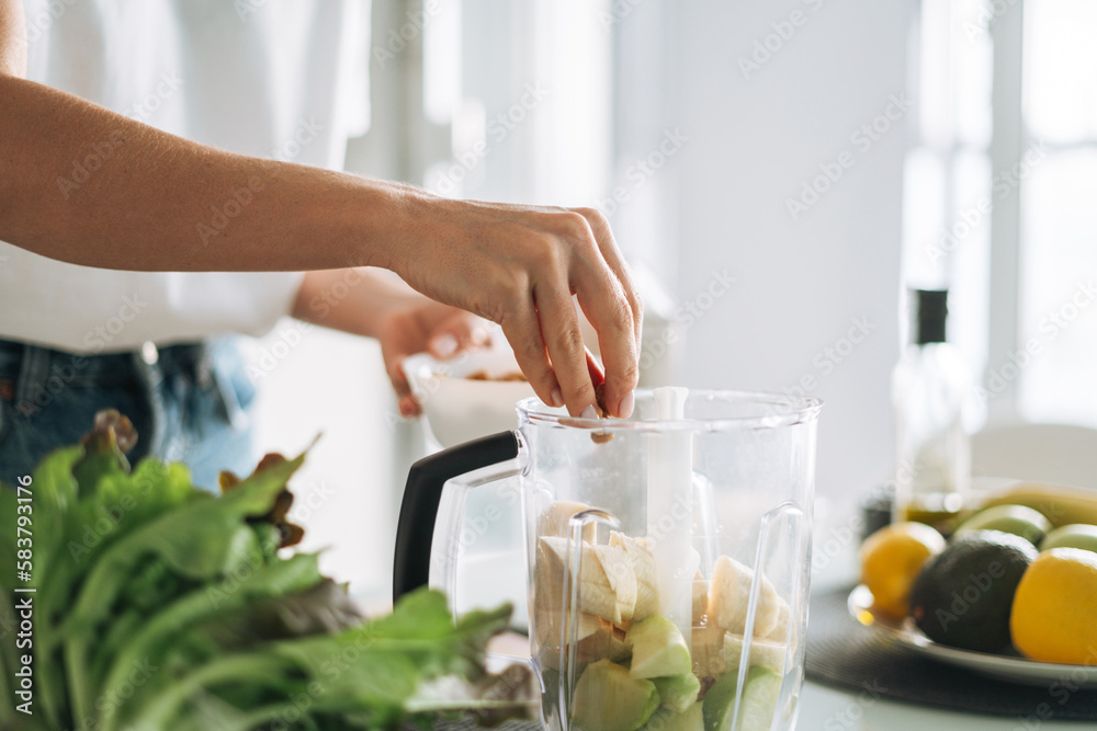 Young slim woman in white t-shirt and blue jeans cooking smoothie healthy food in kitchen at home Young slim woman in white t-shirt and blue jeans cooking smoothie healthy food in kitchen at home