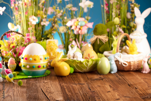 Easter theme. Easter decorations. Easter eggs in basket and easter bunny. Bouquet of spring flowers. Rustic brown table and blue background.