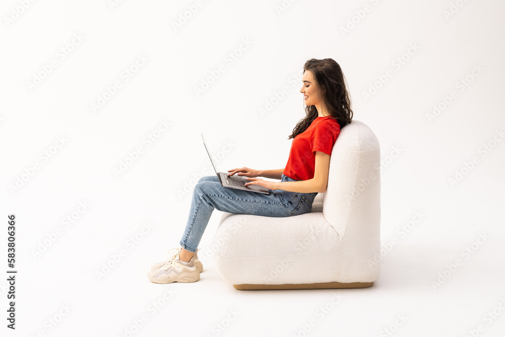Portrait of a smiling young woman sitting in a chair with laptop computer against white background Portrait of a smiling young woman sitting in a chair with laptop computer against white background