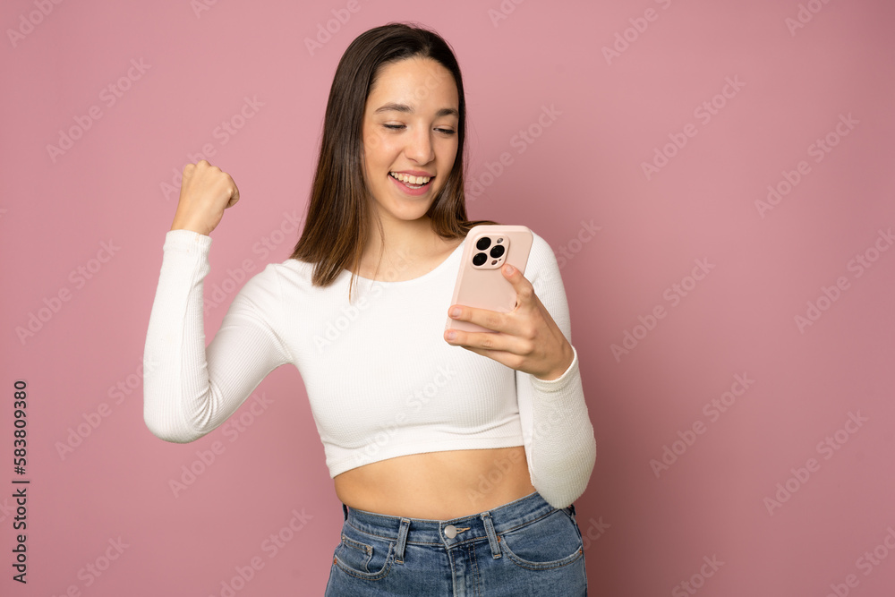 Young woman over isolated pink background with phone in victory position