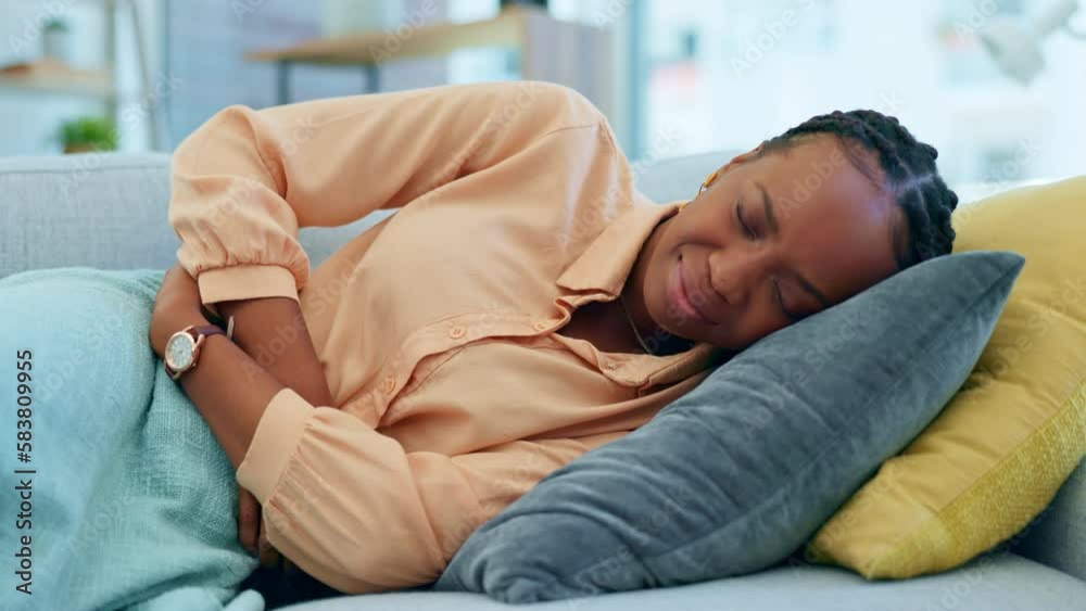 Cramps, stomach ache and woman feeling sick lying on the couch or sofa in a home or house suffering with abdominal pain. Hurt, ill and African American female person touching belly in agony Cramps, stomach ache and woman feeling sick lying on the couch or sofa in a home or house suffering with abdominal pain. Hurt, ill and African American female person touching belly in agony