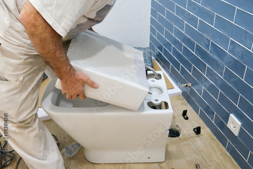 Unrecognizable senior plumber installer installing toilet cistern in a bathroom. photo