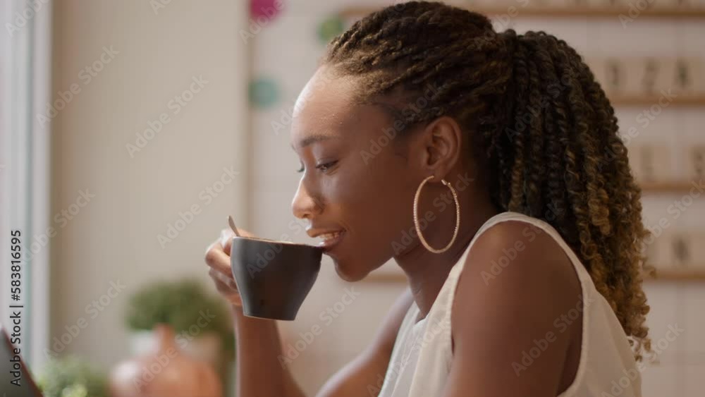 Pretty young black woman drinking coffee while looking at digital tablet in the cafe