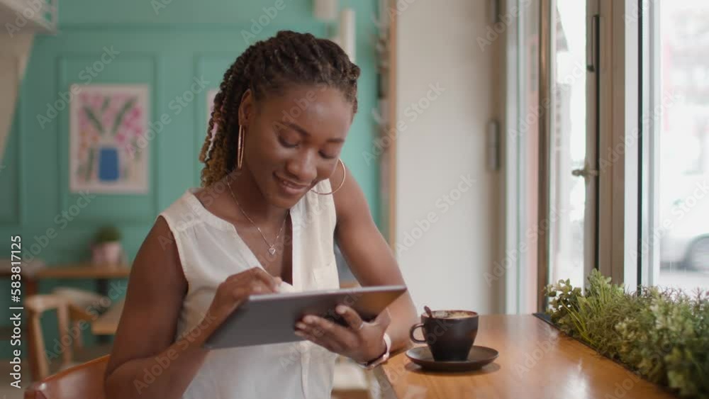 Pretty young black woman drinking coffee while looking at digital tablet in the cafe Pretty young black woman drinking coffee while looking at digital tablet in the cafe