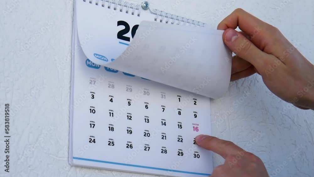 Male hands turns the wall calendar march page 2023 and points a finger
