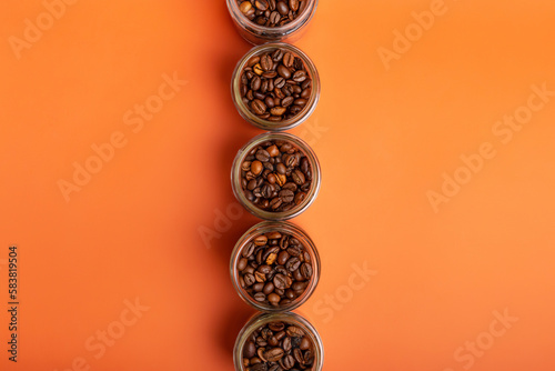 Aromatic roasted arabica and robusta coffee beans in glass small jars on bright orange background. Perfect coffee beans to make tasty coffee beverages such as espresso, americano, cappuccino, latte.