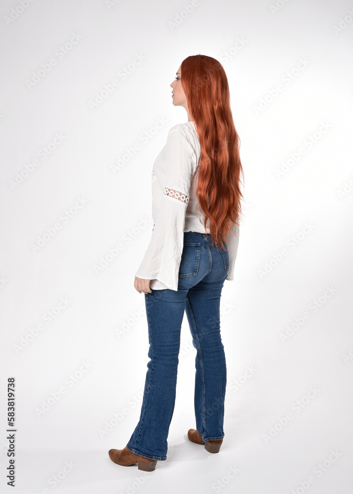 Obraz premium full length portrait of beautiful woman model with long red hair, wearing casual outfit white blouse top and denim jeans, isolated on white studio background. Backwards standing pose, walking away fr