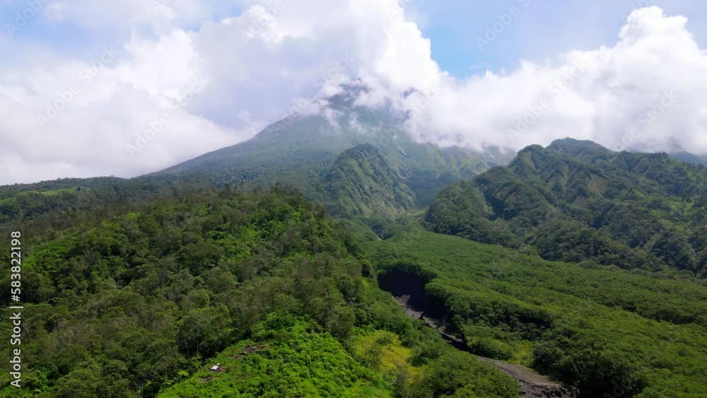 Aerial push out shot of green landscape with Merapi Volcano surrounded by white clouds in Indonesia Aerial push out shot of green landscape with Merapi Volcano surrounded by white clouds in Indonesia