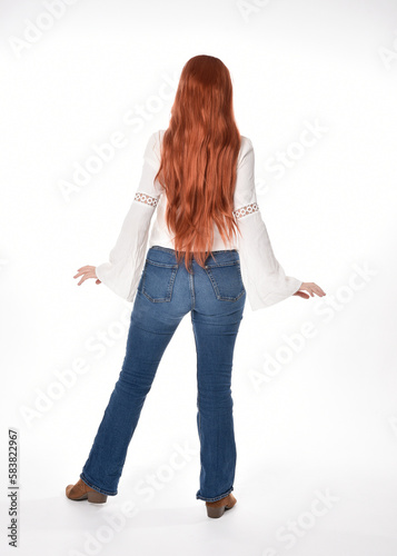 full length portrait of beautiful woman model with long red hair, wearing casual outfit white blouse  top and denim jeans, isolated on white studio background. Backwards standing pose, walking away fr