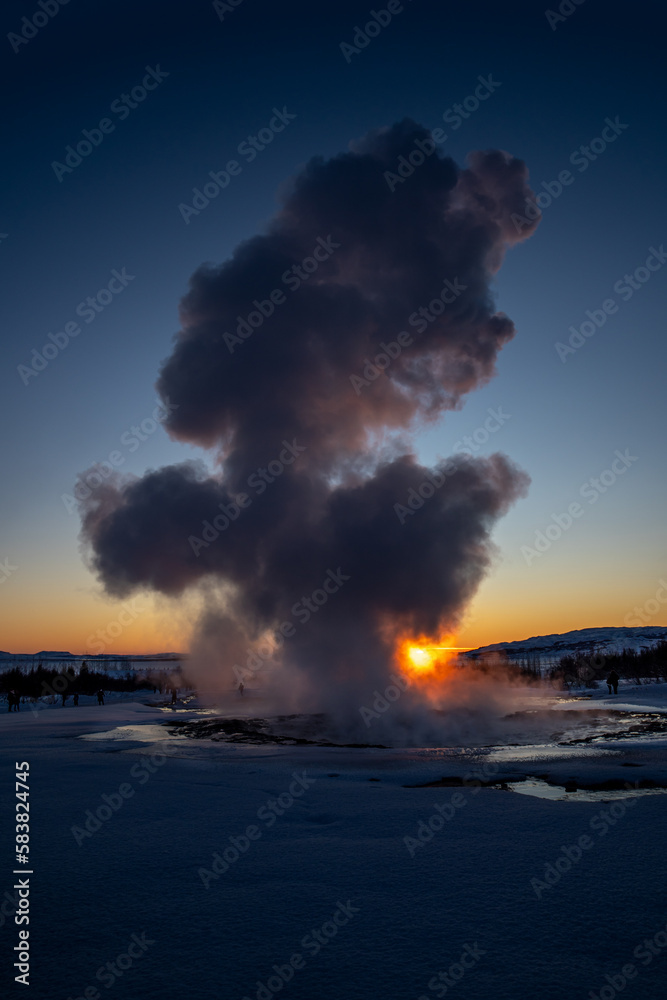 Obraz premium Iceland's great geyser Strokkur in full eruption with mist and smoke backlit and the orange evening or near-dusk sun touching the horizon behind