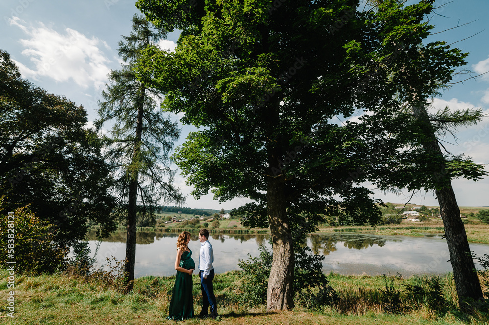 Photo of pregnant happy woman and cheerful man in park. Romantic moments pregnant. Couple walking in nature.