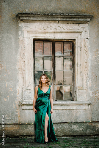 Pregnant woman wearing long green dress walking on the street near old window. New life concept. Waiting baby.