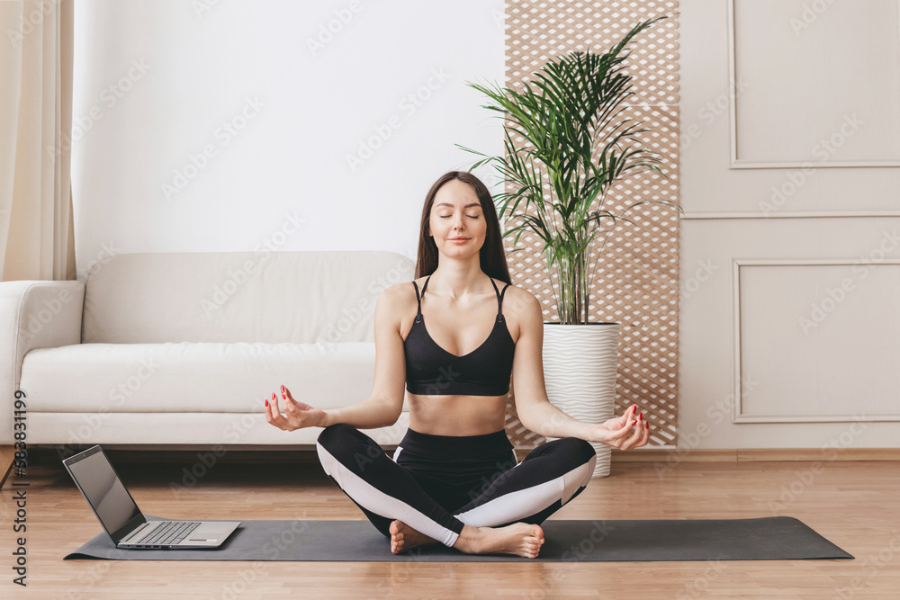 young woman meditates and performs breathing practices with a laptop at home