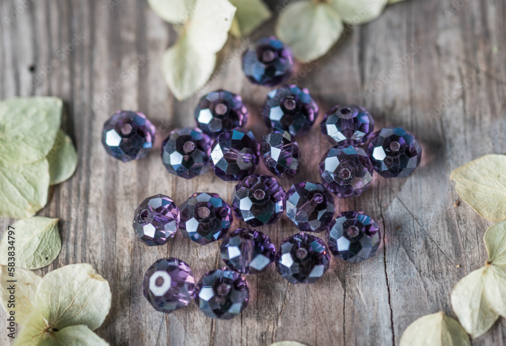 Glass beads of various shapes and sizes are photographed on a wooden board of neutral color. Glass beads of various shapes and sizes are photographed on a wooden board of neutral color.