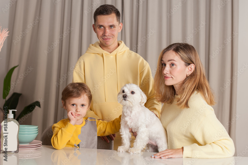 Happy family, parents in yellow sweaters with child son and white dog, three abstract plastic bottles on the table Happy family, parents in yellow sweaters with child son and white dog, three abstract plastic bottles on the table