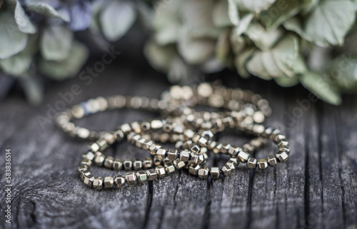 The photo shows hematite beads. This is a natural stone painted in different colors, round and hexagonal. Placed on a wooden board on a background of dried hydrangeas.