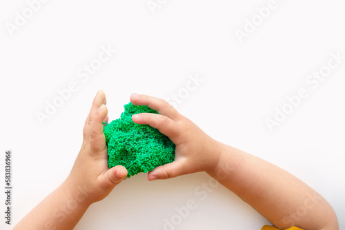 Baby Hands Playing with textured slime with bubbles, stretching the gooey substance on white background. Little child hand holding green shining slime toy, squeezing it to the sides. Top View