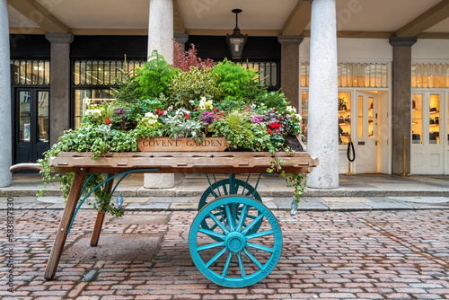 Sticker Old fashioned wooden barrow with boxes of flowers, outside the stores of the world famous Covent Garden Market, London