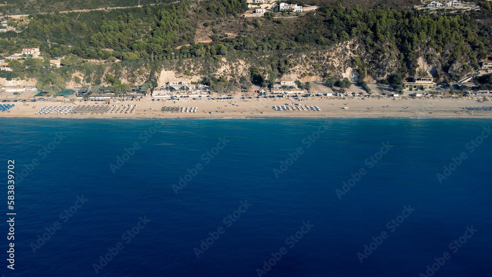 Fototapeta premium Aerial view of beautiful sandy beach with sunshades and soft turquoise ocean wave. Tropical sea in summer season on Kathisma beach on Lefkada island.