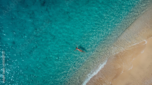 Canvas Print Aerial view of beautiful happy woman in swimsuit laying in the shallow sea water, enjoying sandy beach and soft turquoise ocean wave