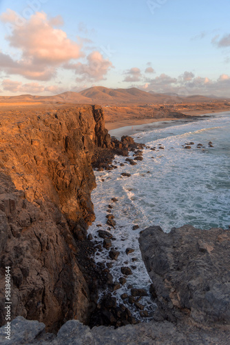 Vista panorámica de la playa de Playa del Castillo desde los acantilados de la playa de arena dorada y el mar turquesa durante la puesta de sol con cielo azul claro en Fuerteventura.