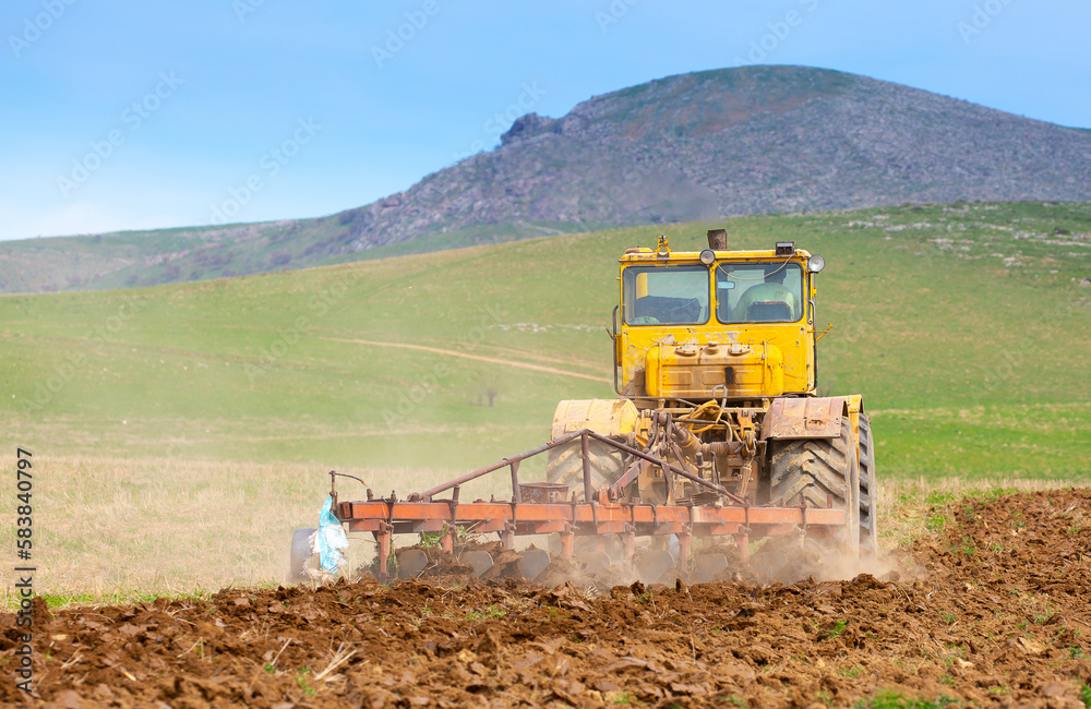 Fototapeta premium Traktok plows the land, preparing for sowing seeds. Industrial agriculture and farming. Tractor driver at work in the field. Harvesting, harvester harvests.