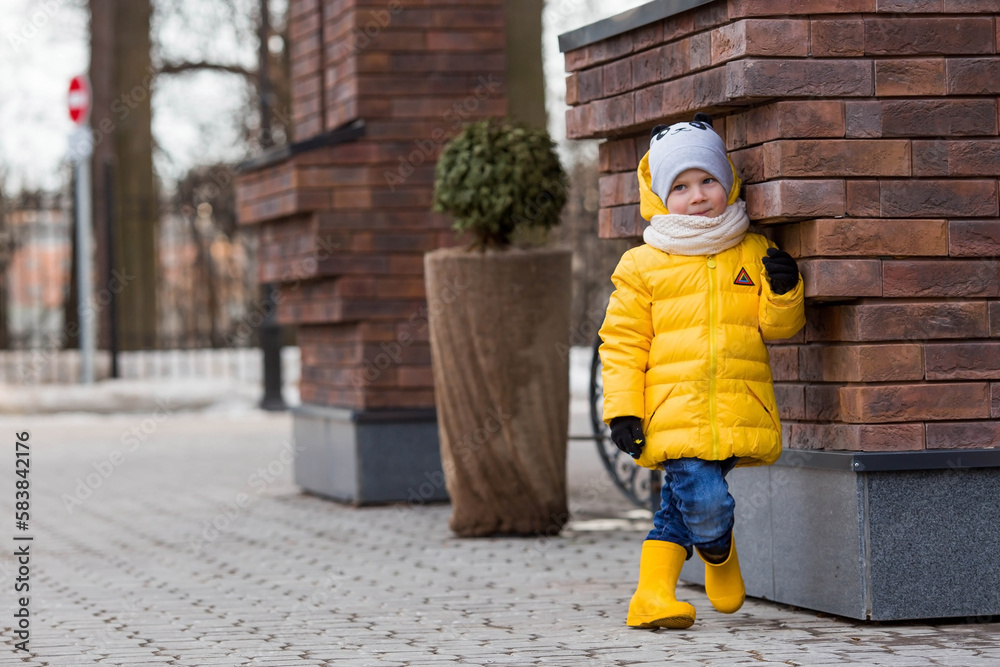 Portrait of a small child 4 years old in yellow rubber boots and a jacket. The kid walks in the park in the spring. Photo of spring and autumn holidays.